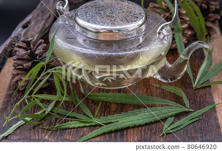 Cannabis herbal tea in teapot and Stem with green marijuana leaves on wooden background. 80646920