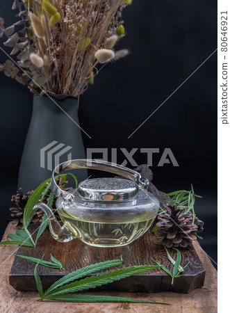 Cannabis herbal tea in teapot and Stem with green marijuana leaves on wooden background. Cannabis herbal tea in teapot and Stem with green marijuana leaves on wooden background. 80646921