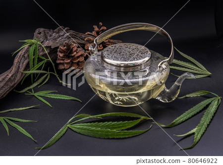 Cannabis herbal tea in teapot and Stem with green marijuana leaves on black background. 80646922