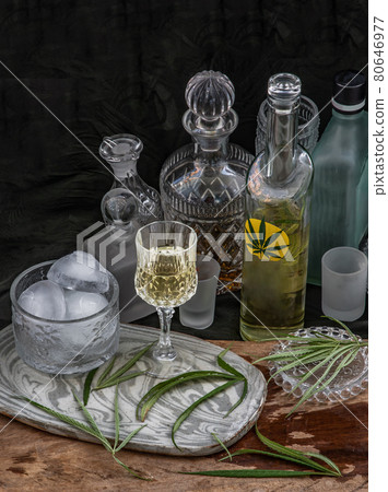 Ice cold Marijuana cannabis CBD infused drink in a crystal clear glass with green marijuana leaf on wooden background. Ice cold Marijuana cannabis CBD infused drink in a crystal clear glass with green marijuana leaf on wooden background. 80646977