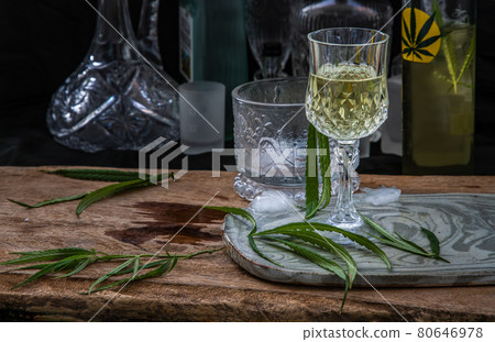 Ice cold Marijuana cannabis CBD infused drink in a crystal clear glass with green marijuana leaf on wooden background. Ice cold Marijuana cannabis CBD infused drink in a crystal clear glass with green marijuana leaf on wooden background. 80646978