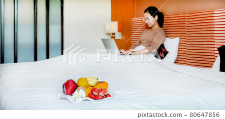 Fruits in tray in front of tourists used laptop on the bed in the luxury hotel room 80647856