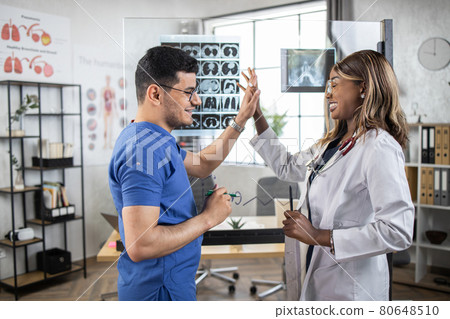 Multiethnic doctors analyzing x ray tomography scan of patient lungs, giving high five Multiethnic doctors analyzing x ray tomography scan of patient lungs, giving high five 80648510