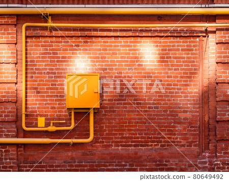 Red brick wall with yellow gas pipes and sunbeams. Old wall with sun reflections. Old building with shabby surface. 80649492