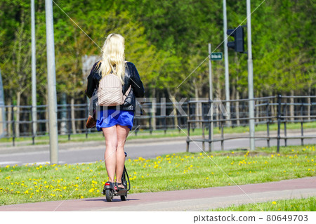 a woman with long blonde hair and a short blue skirt rides an electric scooter 80649703