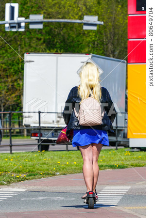 a woman with long blonde hair and a short blue skirt rides an electric scooter a woman with long blonde hair and a short blue skirt rides an electric scooter 80649704