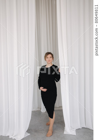 Pregnant woman in black dress walk through the white curtains 80649811