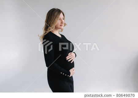 Elegant pregnant woman in black dress tup hands on belly and smile. White background 80649870