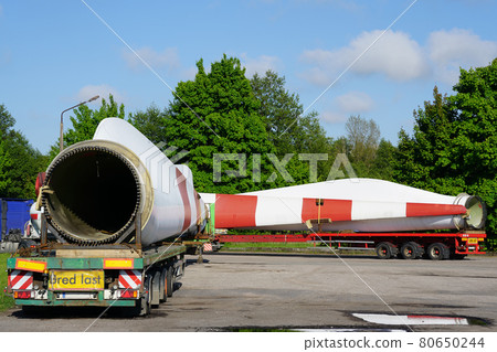 A view of a truck, a low-loader semi-trailer with oversized wind generator parts in the parking lot 80650244