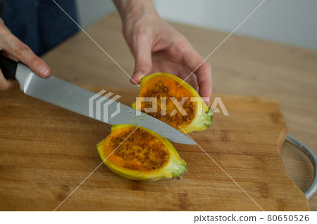 Female hands is cutting a fresh ripe cactus pear on a cut wooden board. Exotic fruits, healthy eating concept. Female hands is cutting a fresh ripe cactus pear on a cut wooden board. Exotic fruits, healthy eating concept. 80650526