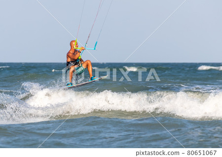 Young adult caucasian fit male person enjoy riding kite surf board making extreme trick stunt bright sunny day against blue sky at sea or ocean shore. Watersport adrenaline fun adventure acitivity 80651067