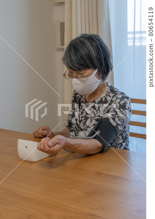 Elderly Japanese woman measuring blood pressure while wearing a mask 80654119