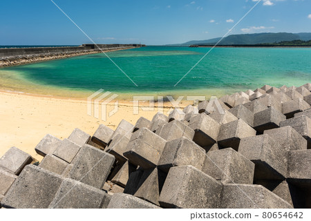 Amazing tropical town beach, crystal clear dark emerald green sea, smooth sands, long pier, tide blocks, blue sky, mountains. Iriomote Island. Amazing tropical town beach, crystal clear dark emerald green sea, smooth sands, long pier, tide blocks, blue sky, mountains. Iriomote Island. 80654642