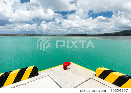 Impressive emerald green sea, wavy surface due to a gentle wind, long pier, blue sky clouds, red mooring bollard at Uehara port. Iriomote Island. Impressive emerald green sea, wavy surface due to a gentle wind, long pier, blue sky clouds, red mooring bollard at Uehara port. Iriomote Island. 80654867