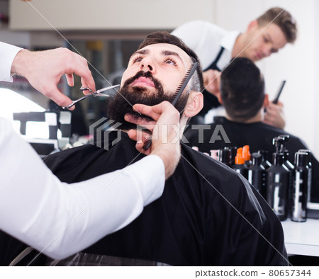 Glad stylist creating shape for beard of client Glad stylist creating shape for beard of client 80657344