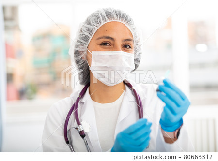 Female health worker prepares a syringe for injection in the treatment room Female health worker prepares a syringe for injection in the treatment room 80663312