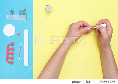 Woman covers her nails with protective varnish. Colored background. Care nails. Tools for manicure and pedicure. SPA. Woman covers her nails with protective varnish. Colored background. Care nails. Tools for manicure and pedicure. SPA. 80665126