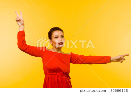 Beautiful woman in red dress pointing finger on yellow background Beautiful woman in red dress pointing finger on yellow background 80666128