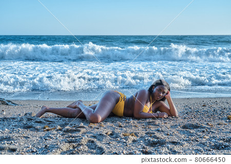 African American woman lying on the sand on the beach with sea waves in the background African American woman lying on the sand on the beach with sea waves in the background 80666450