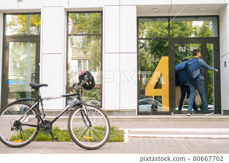 Courier male with large thermo backpack delivered an online order on the bicycle, calling on intercom on house wall. Courier male with large thermo backpack delivered an online order on the bicycle, calling on intercom on house wall. 80667702