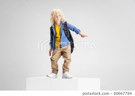 Cute little curly preschool boy in casual clothes stands on large box isolated over white studio background. 80667784