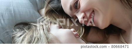 Mom and daughter laugh and look at each other while lying in bed 80668471