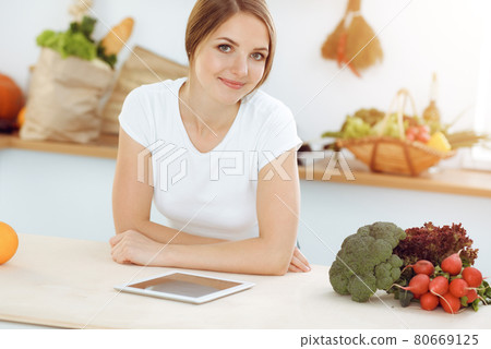 An attractive young woman looking for a new recipe for a delicious salad mix while sitting at the table in sunny kitchen. Tablet pc is the best cookbook An attractive young woman looking for a new recipe for a delicious salad mix while sitting at the table in sunny kitchen. Tablet pc is the best cookbook 80669125