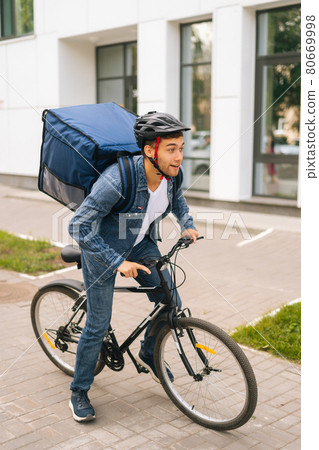 Full length vertical portrait of cheerful handsome young delivery man in protective helmet starting bike ride in city street. Full length vertical portrait of cheerful handsome young delivery man in protective helmet starting bike ride in city street. 80669998