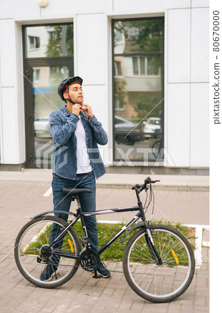 Full length vertical portrait of handsome young man putting helmet on head before going to go ride by bicycle in city street. Full length vertical portrait of handsome young man putting helmet on head before going to go ride by bicycle in city street. 80670000