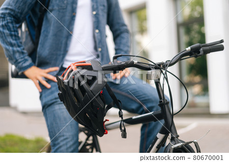 Close-up cropped shot of bicycle helmet hanging on handlebars of bike standing in city street summer day on blurry background Close-up cropped shot of bicycle helmet hanging on handlebars of bike standing in city street summer day on blurry background 80670001