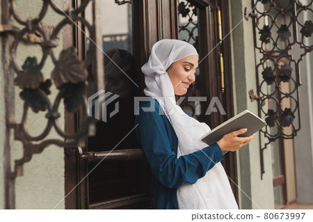 Portrait of young muslim woman wearing hijab reading book outdoors Portrait of young muslim woman wearing hijab reading book outdoors 80673997