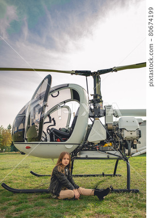 Tween girl sitting on green grass of flying field near helicopter 80674199