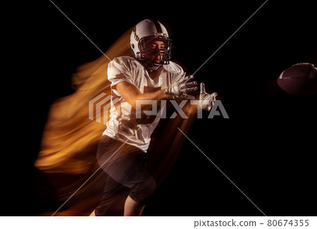 Portrait of young man, American football player training isolated on dark studio background with mixed neon light. Concept of sport, competition and beauty Portrait of young man, American football player training isolated on dark studio background with mixed neon light. Concept of sport, competition and beauty 80674355