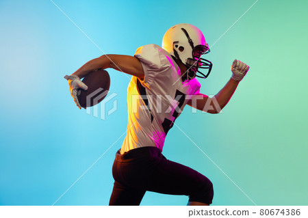 Portrait of American football player training isolated on blue studio background in neon light. Concept of sport, competition Portrait of American football player training isolated on blue studio background in neon light. Concept of sport, competition 80674386