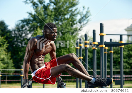 Black fitness man exercising dips, cross training of male model in urban environment. An African guy in his twenties is training on the street. 80674651