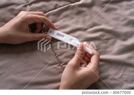 Hand holds a test cartridge at home. COVID-19 Ag rapid self test kits on bed at home in quarantine. Antigen or Antibody test. Virus disease healthcare check. Coronavirus outbreak. 80677000