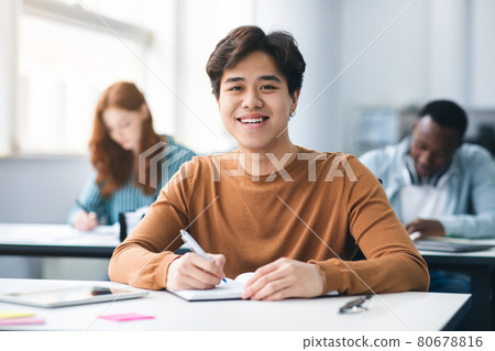 Asian male student sitting at desk writing in classroom 80678816