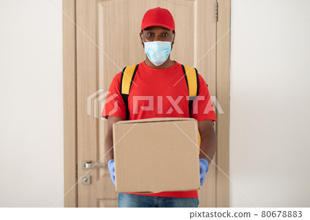 Black delivery man in medical mask and gloves holding parcel Black delivery man in medical mask and gloves holding parcel 80678883
