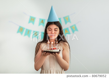 Joyful Indian teen girl in birthday hat blowing candles on cake at home 80679052