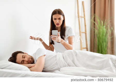 Shocked Woman Reading Cheating Husband's Messages On Cellphone In Bedroom Shocked Woman Reading Cheating Husband's Messages On Cellphone In Bedroom 80679492
