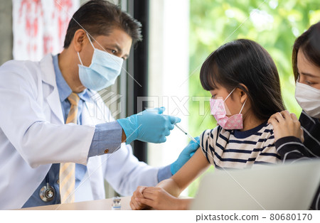 Asian senior doctor wearing gloves and isolation mask is making a COVID-19 vaccination in the shoulder of child patient with her mother at hospital. Asian senior doctor wearing gloves and isolation mask is making a COVID-19 vaccination in the shoulder of child patient with her mother at hospital. 80680170