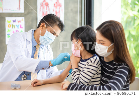 Asian senior doctor wearing gloves and isolation mask is making a COVID-19 vaccination in the shoulder of child patient with her mother at hospital. Asian senior doctor wearing gloves and isolation mask is making a COVID-19 vaccination in the shoulder of child patient with her mother at hospital. 80680171