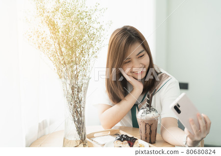 beautiful girl smiling using mobile phone selfie in the cafe, girl eat coffee and cake 80680824