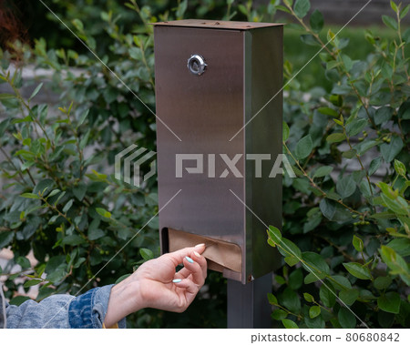 Close-up of a woman pulls out a paper bag from a dog waste station Close-up of a woman pulls out a paper bag from a dog waste station 80680842