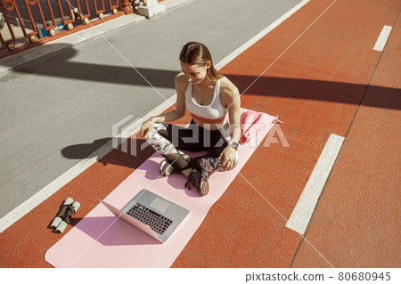 Sportive woman watches video tutorial via laptop sitting on footbridge Sportive woman watches video tutorial via laptop sitting on footbridge 80680945