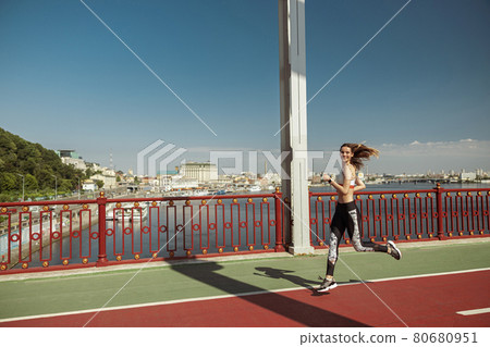 Sportswoman with flying hair runs along footbridge on sunny day Sportswoman with flying hair runs along footbridge on sunny day 80680951