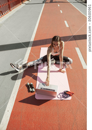 Sportswoman in tracksuit prepares for training with modern laptop on footbridge Sportswoman in tracksuit prepares for training with modern laptop on footbridge 80680961