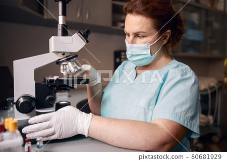 Woman lab assistant works with microscope to research material sample in clinic 80681929