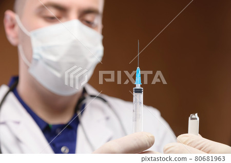 Young caucasian male doctor in a white coat holding a syringe with a vaccine. Focus on the syringe 80681963