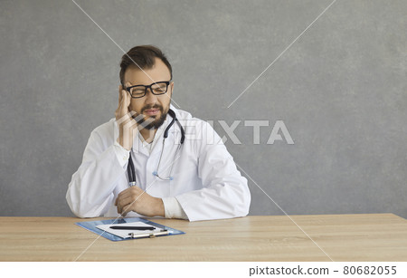 Young doctor having a bad headache caused by tiredness and lots of stress at work Young doctor having a bad headache caused by tiredness and lots of stress at work 80682055